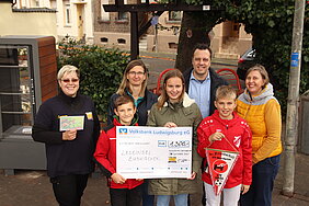 Bürgermeister Sacha Reichelt und Melanie Barth stehen gemeinsam mit Erwachsenen und Kindern aus Horrheim und einem Scheck über 1300 Euro auf dem Luisenplätzchen. 