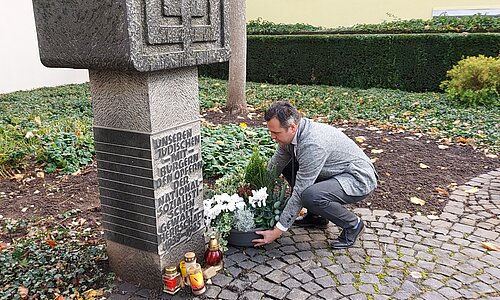 Bürgermeister Sacha Reichelt stellt eine Pflanzschale an der Gedenkstätte der jüdischen Synagoge ab