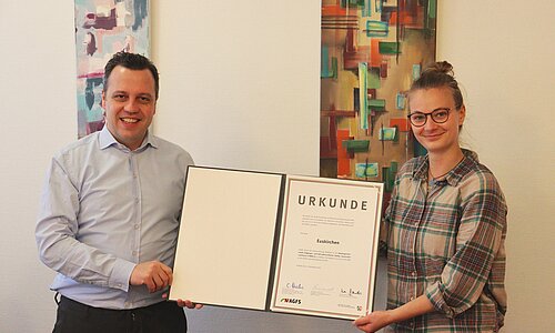 Euskirchens Bürgermeister und eine Mitarbeiterin zeigen eine Urkunde in die Kamera.